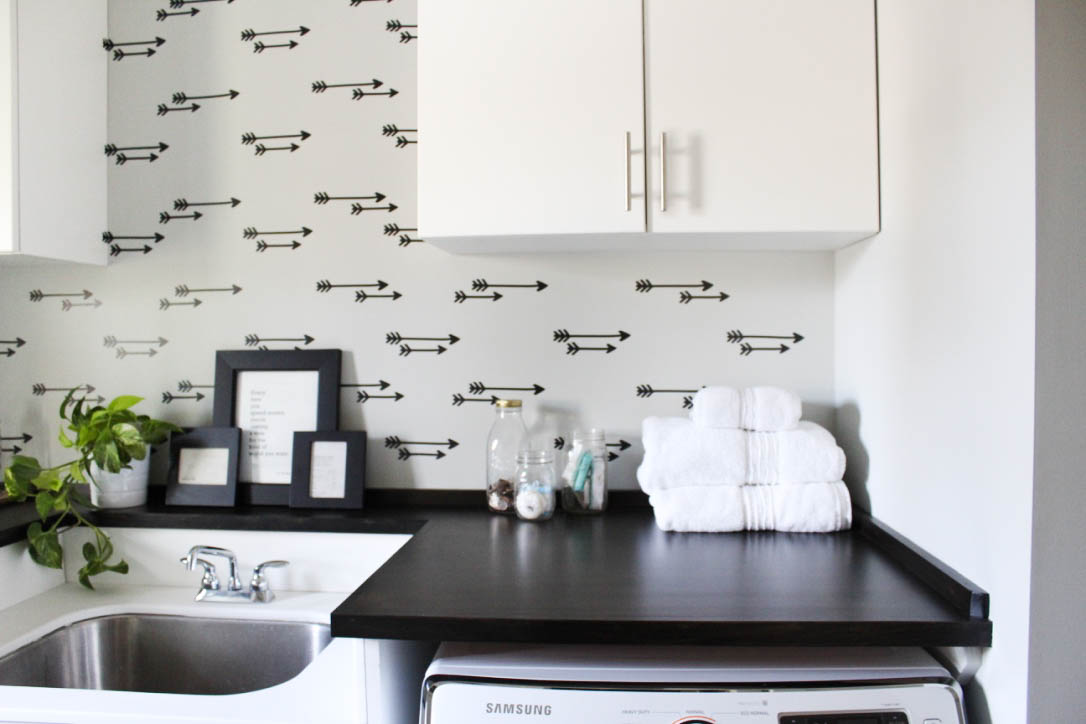 Laundry room decor featuring a faux arrow wallpaper accent wall with stacked white towels.