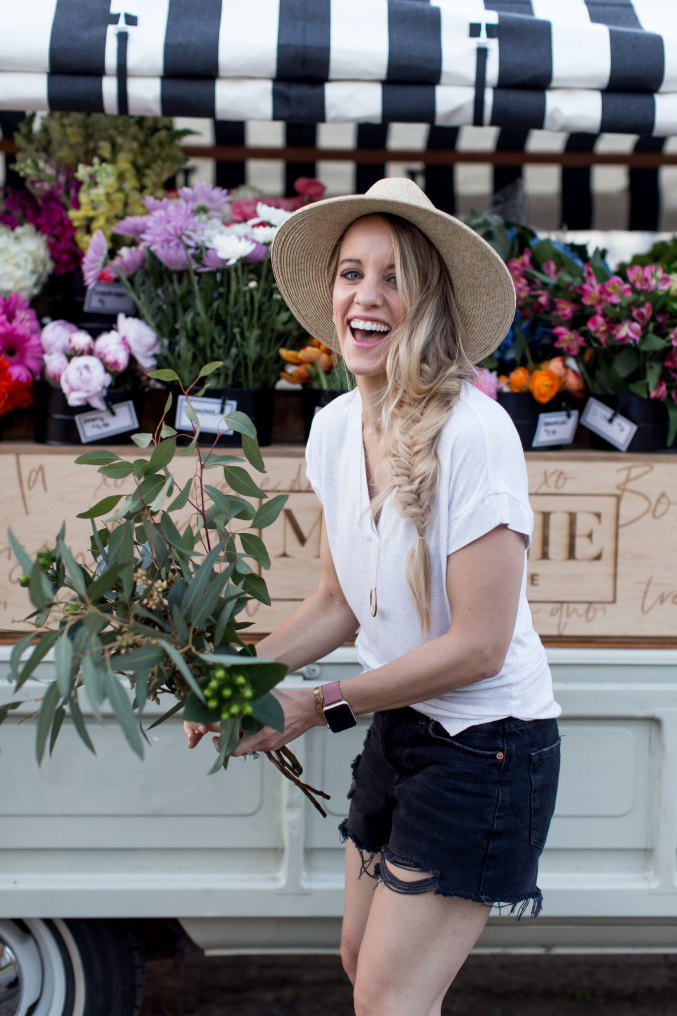 summer outfit for a casual day. blonde girl with fishtail braid and straw hat in front of majolie flower truck in black shorts, white top and black peep toe shoes