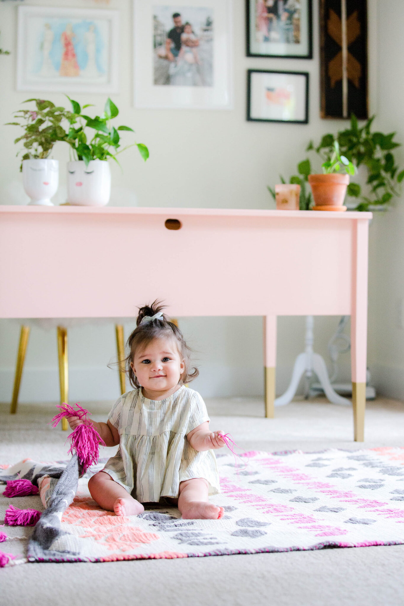 Baby sitting in front of pink desk on bright patterned rug