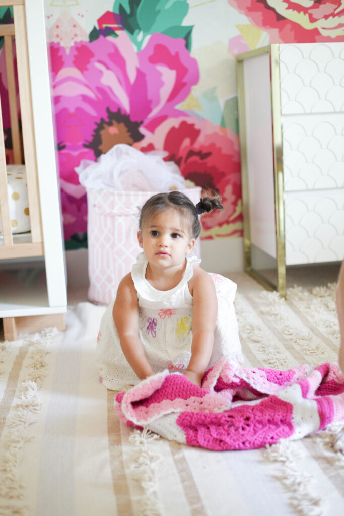 Toddler in bright floral room with light rug and scalloped dresser