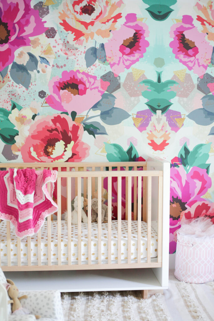 Light wood crib with bright floral wallpaper wall