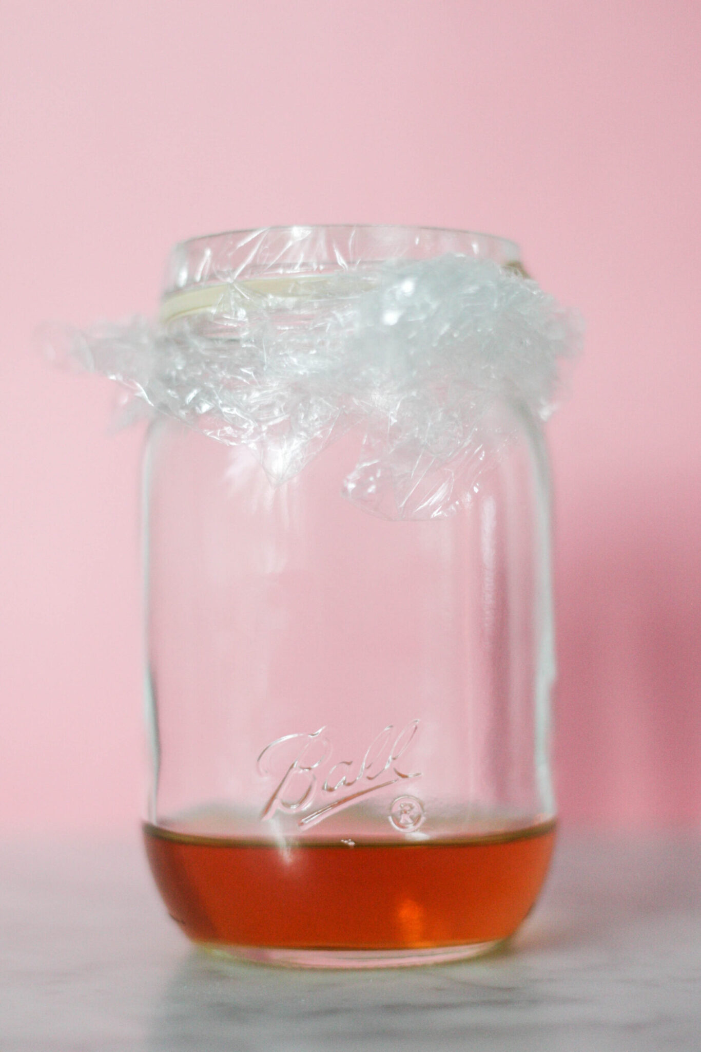 A mason jar with vinegar topped with plastic wrap to get rid of fruit flies.