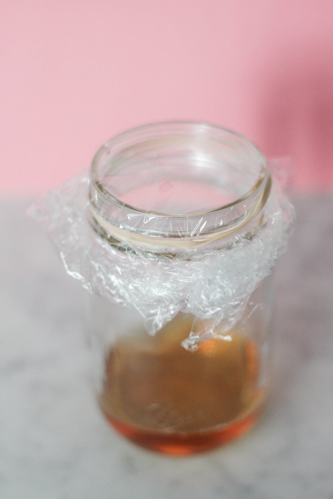 A mason jar with vinegar topped with plastic wrap to get rid of fruit flies.