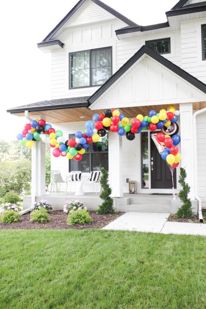Multi-colored balloon garland with superhero balloons on outside of house for superhero birthday party