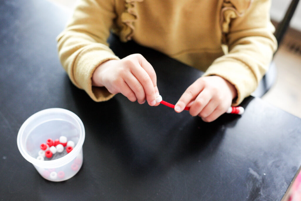 Toddler putting beads on red pipe cleaner
