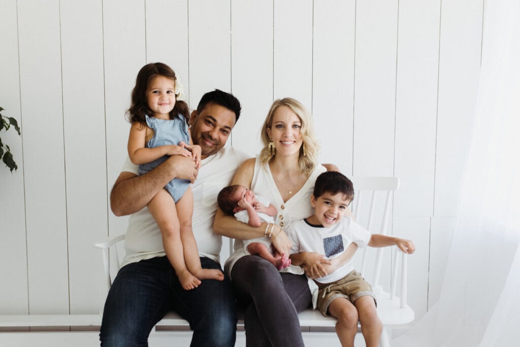 A family with a new baby in casual clothes in front of white background