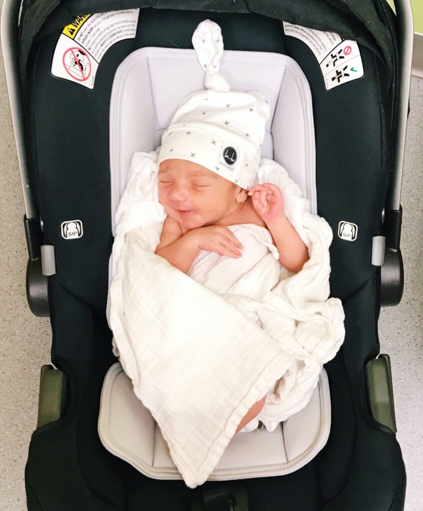 Baby wrapped in swaddle cloth and hat in car seat