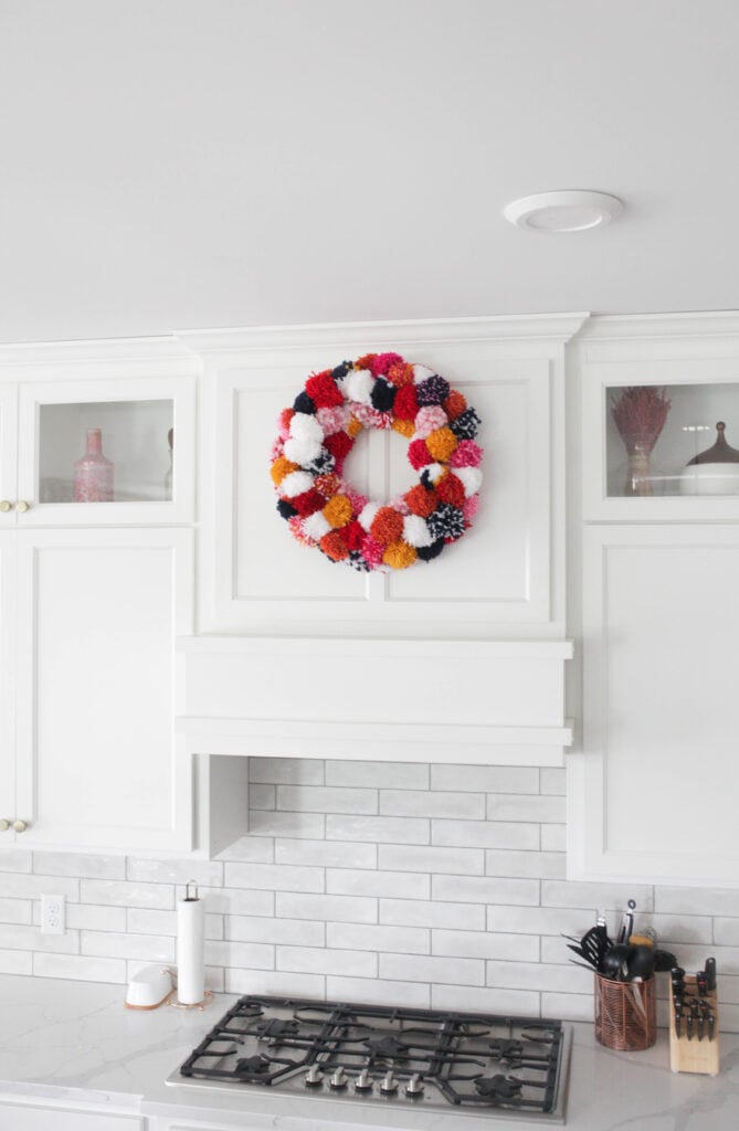 pom pom wreath hanging on vent hood in white kitchen