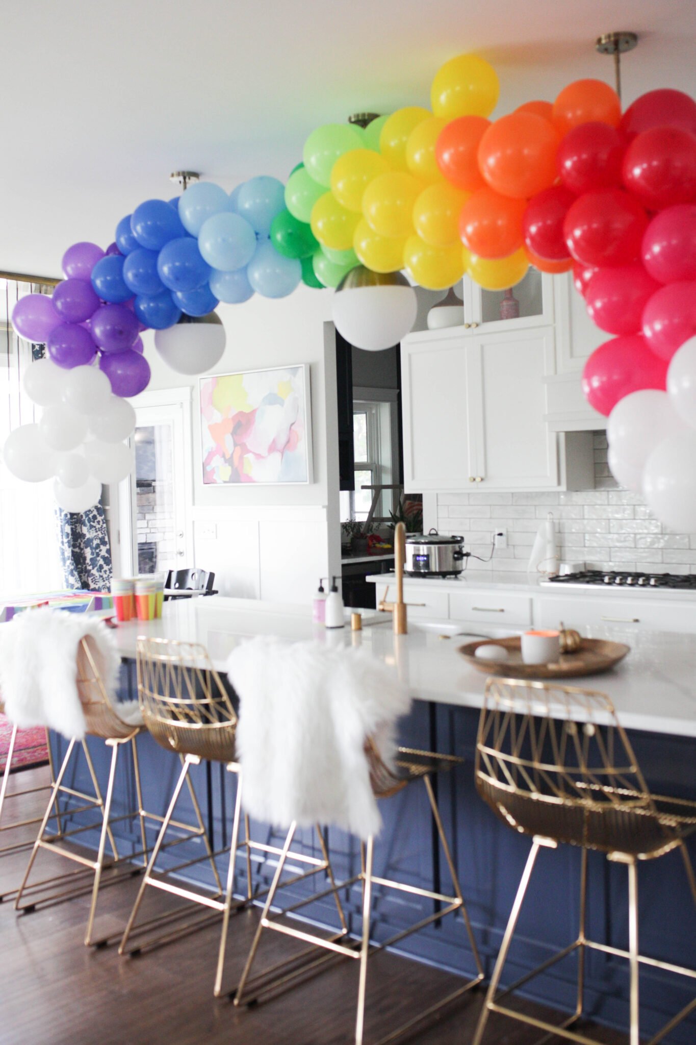 Rainbow balloon garland over kitchen island. Groups of each color with white on the ends to look like clouds