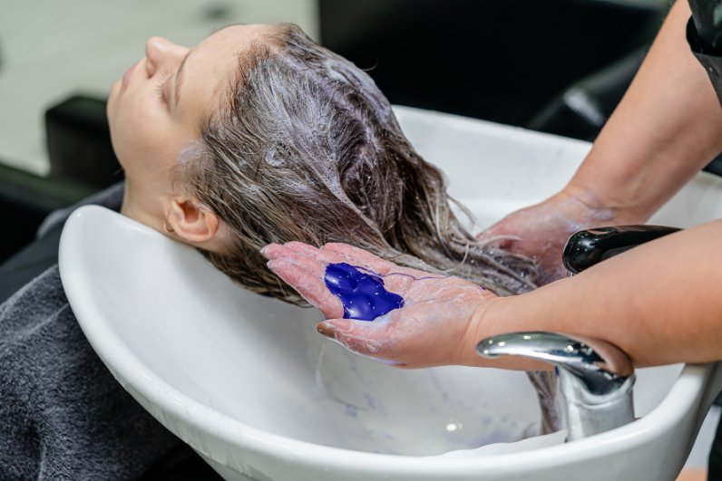 Woman getting hair washed at salon with purple shampoo