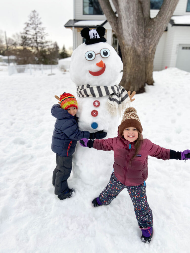 2 kids in front of a snowman