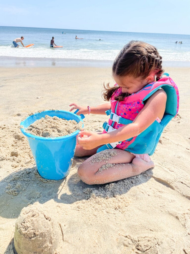 toddler on the beach playing with sand in bucket