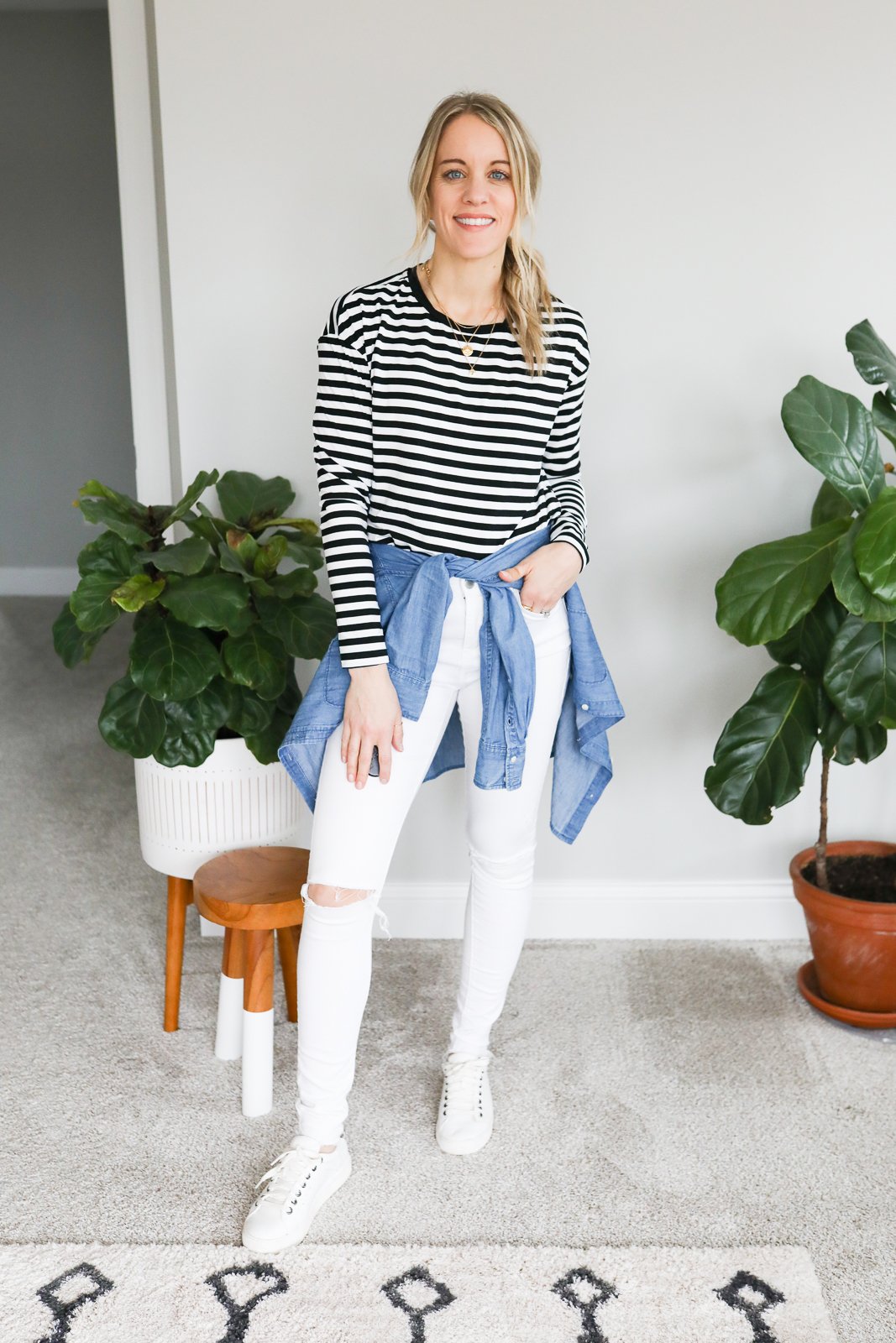 woman in stripe top, white jeans and white sneakers and chambray top tied around waist