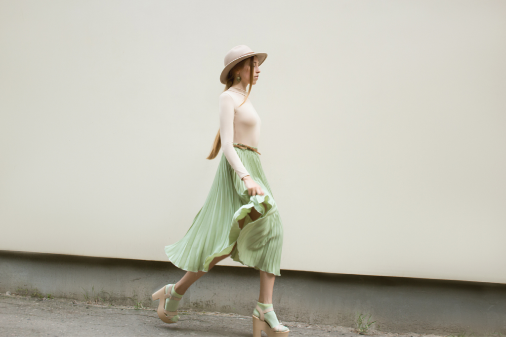 Woman wearing green Knife Pleated Skirt with white top and green sock, tan sandals and hat