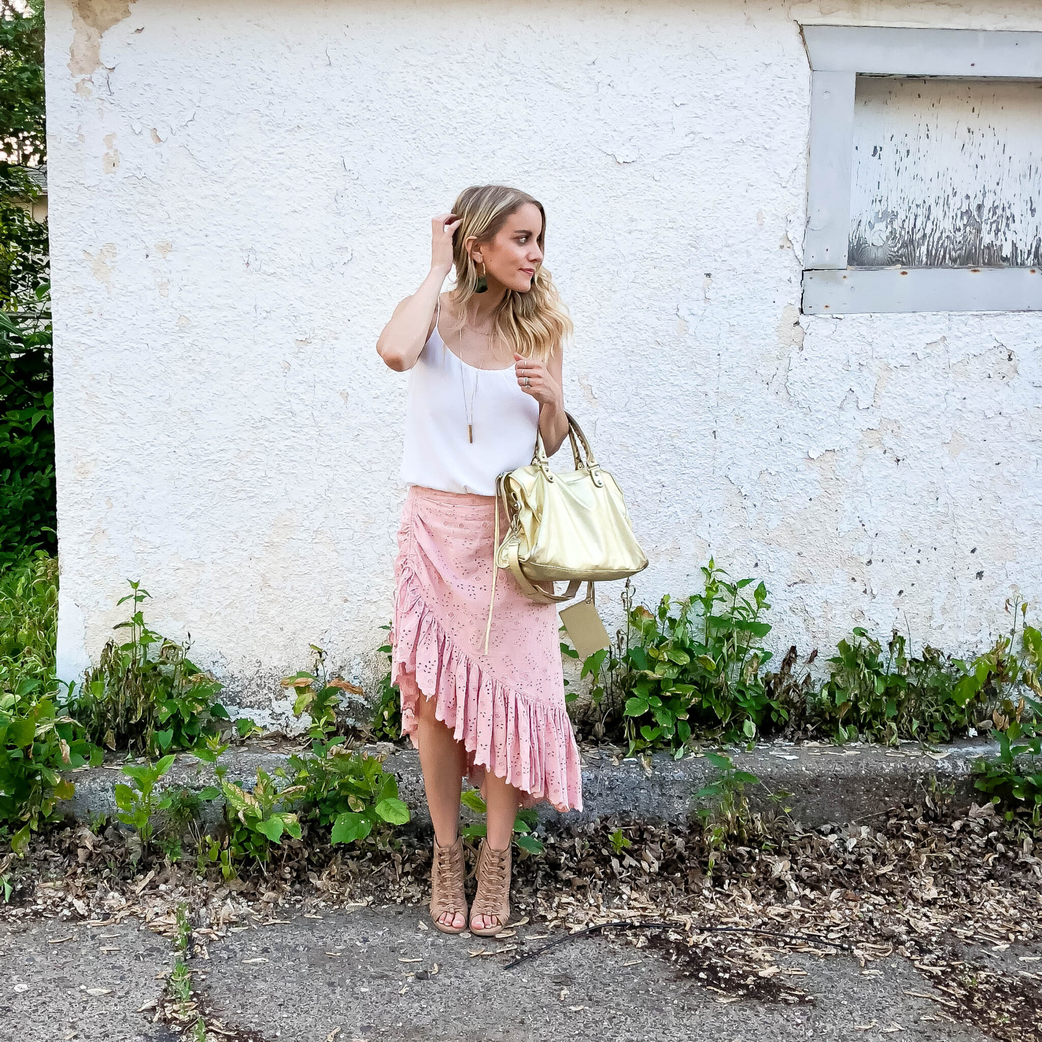 Woman wearing pink asymmetrical skirt, white top, gold balenciaga bag