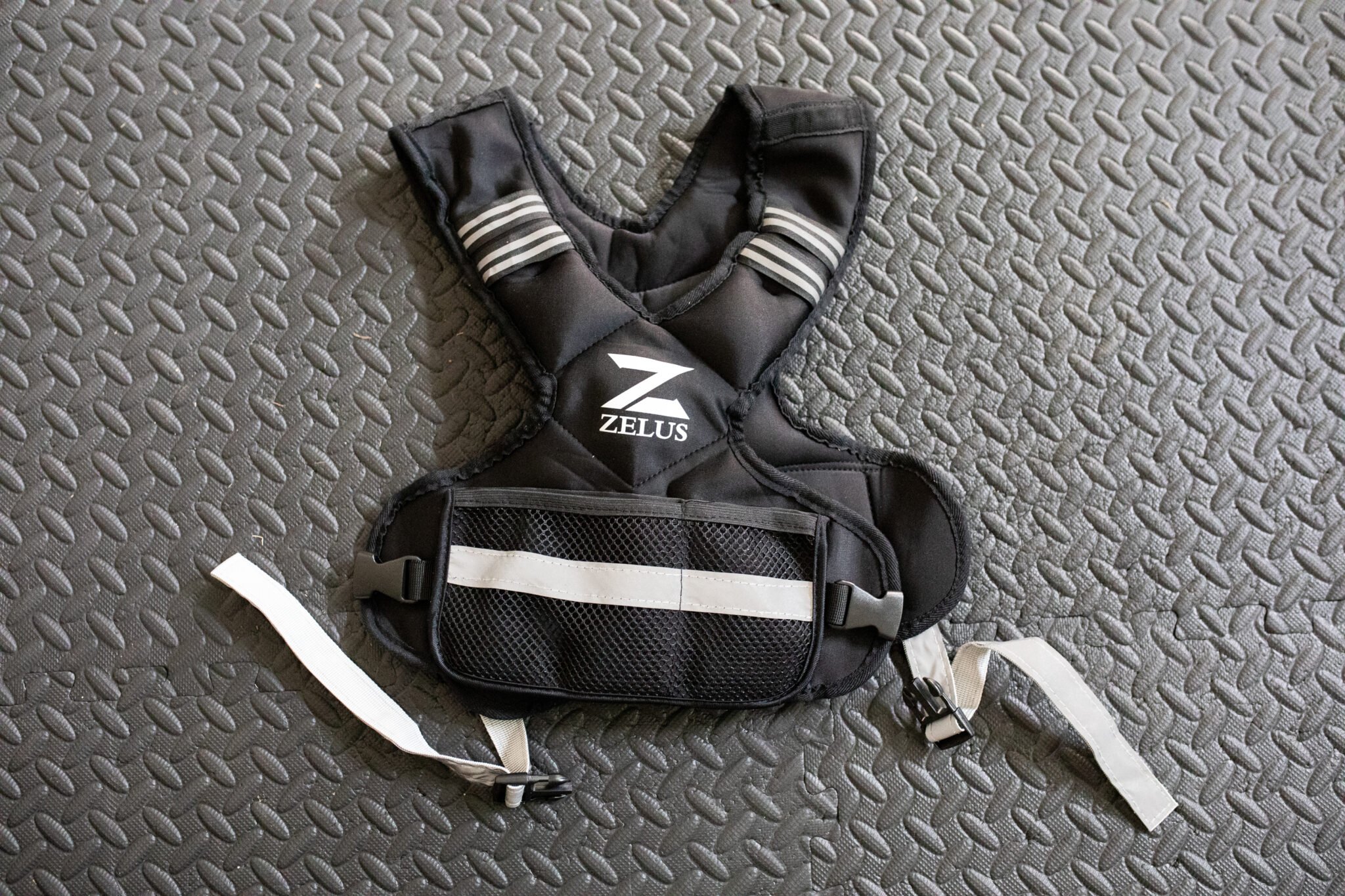 Black ZELUS adjustable weighted workout vest on top of gym mats