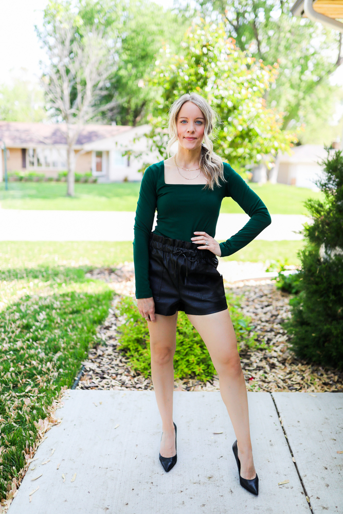woman wearing faux leather shorts and green bodysuit