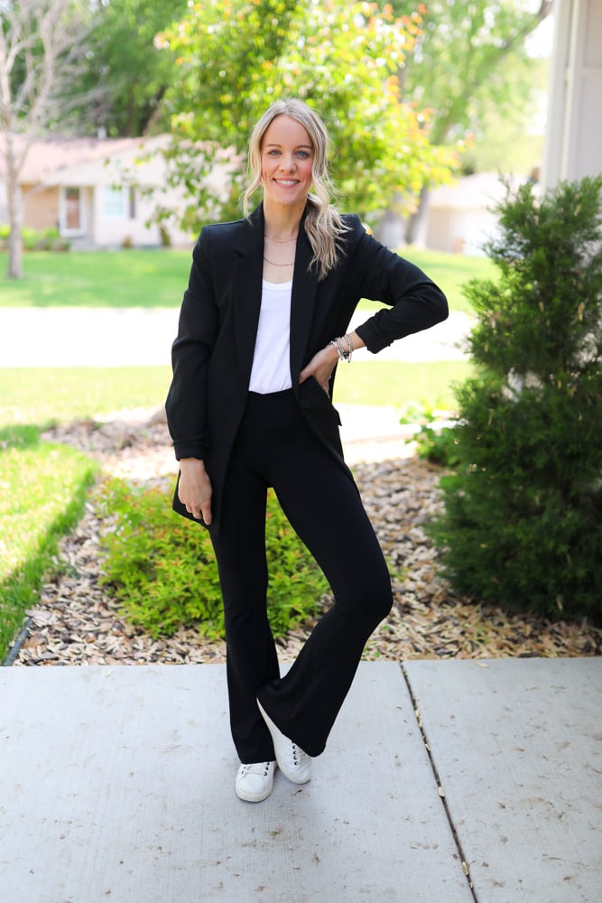 Woman wearing flare leggings with white top, black blazer and white sneakers and crossbody bag.