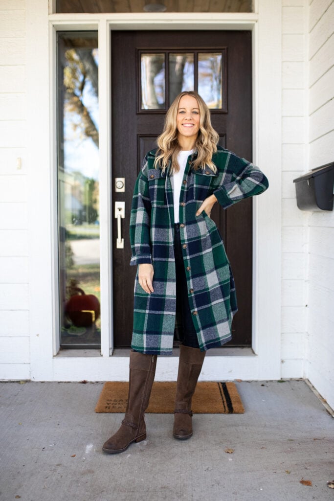 a woman standing in front of a door with a long green plaid shacket, riding boots and skinny jeans
