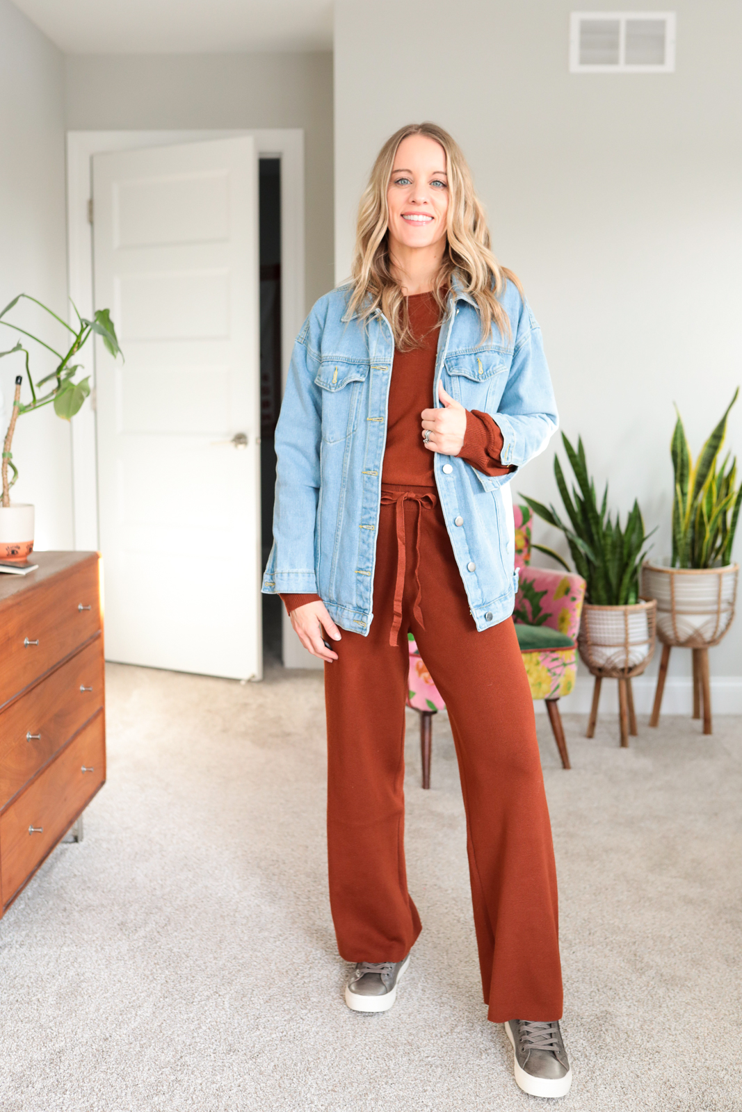 woman wearing rust colored lounge set with denim jacket and taos sneakers
