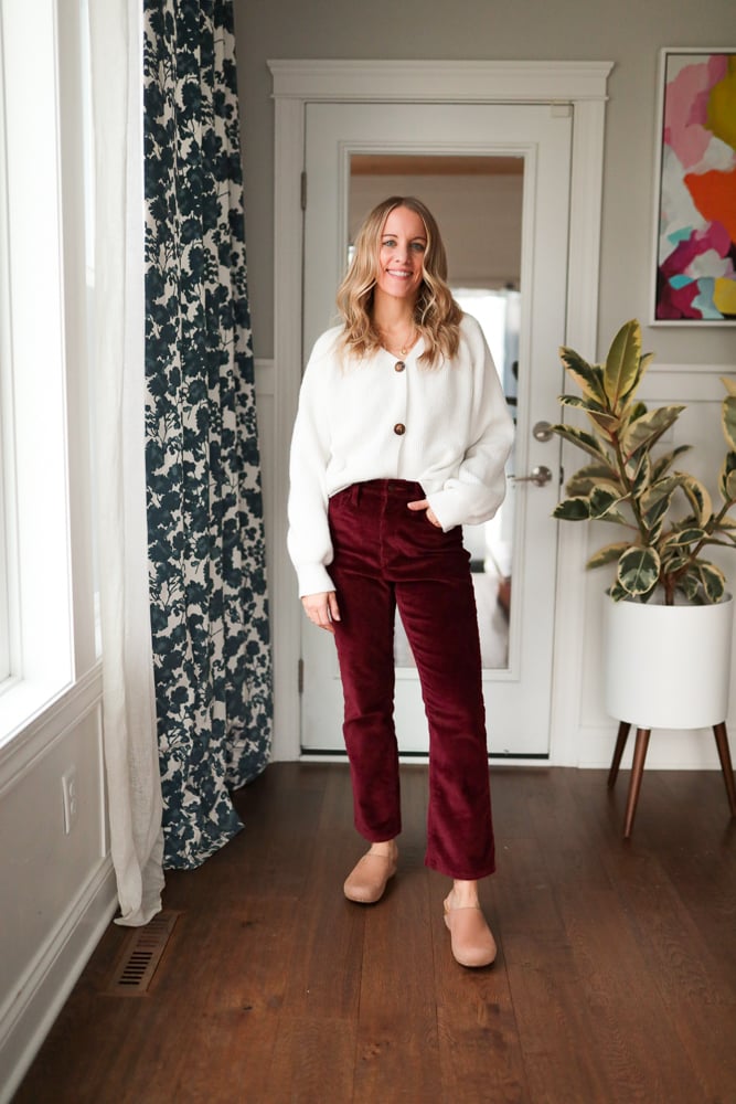 Woman wearing burgundy pants and white button down cardigan and clogs