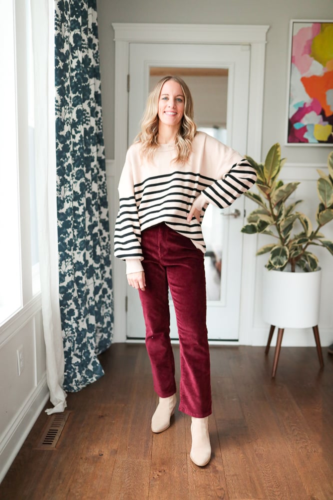 Woman wearing burgundy pants and tan and black striped sweater.