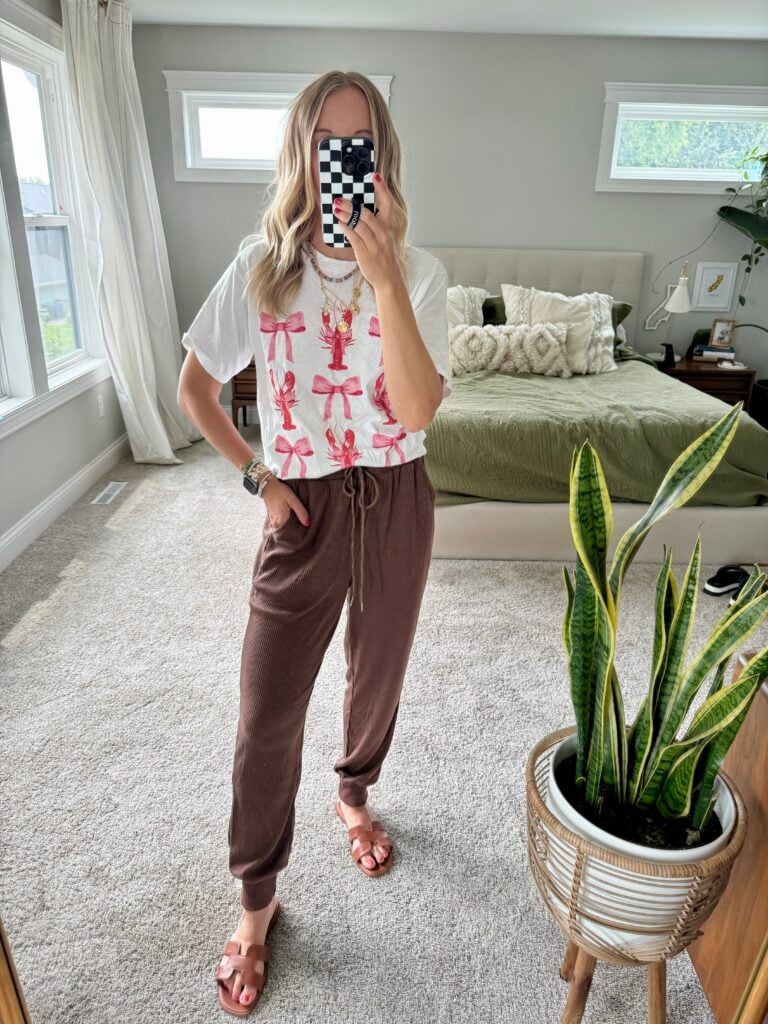 Woman in brown pants and graphic tee with lobster and bows.