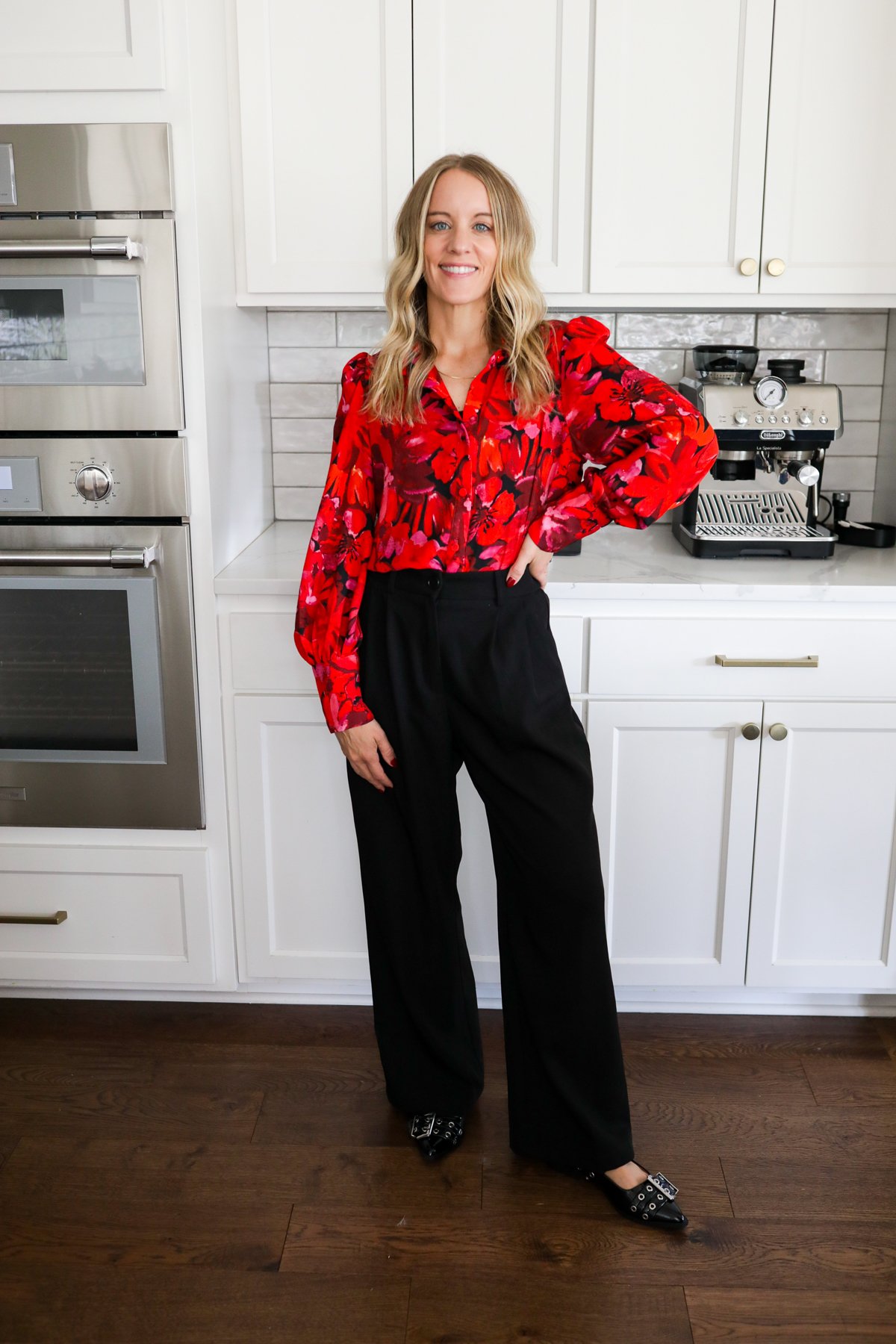 Woman in black trousers, a black tank and red blouse standing in a kitchen.