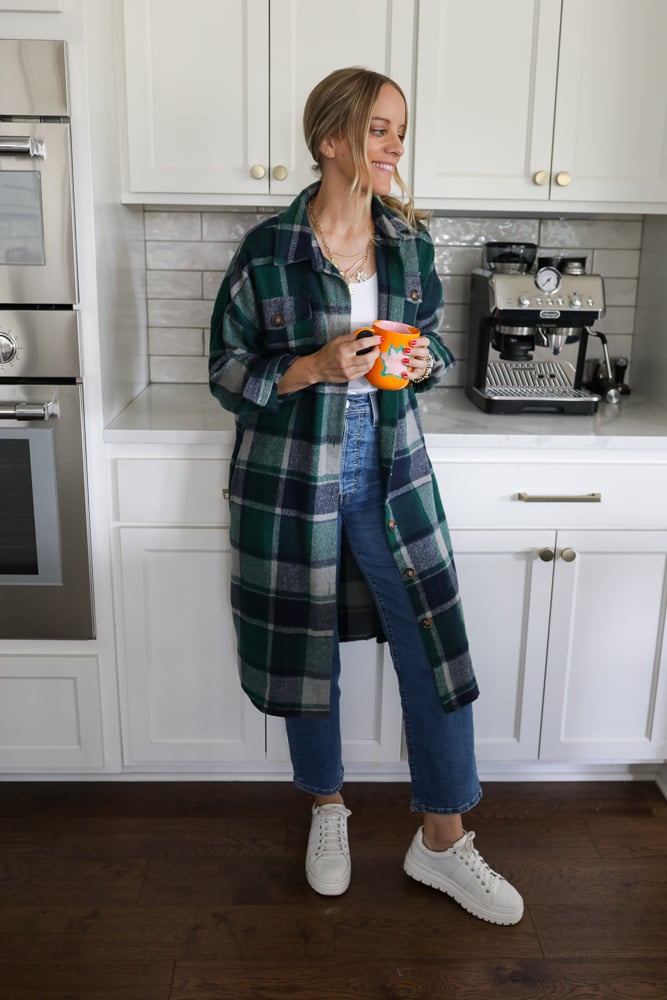 Woman in jeans, a white tank and long duster style shacket.