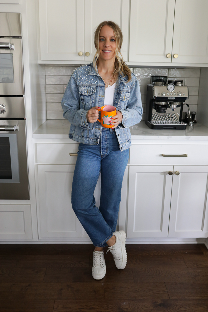 Woman in jeans, a white tank and denim jacket with pearls.