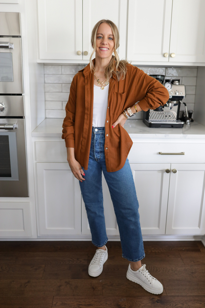 Woman in jeans, a white tank and tan waffle knit button down.