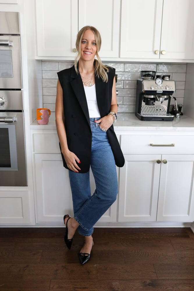 Woman in jeans, a white tank and oversized vest.