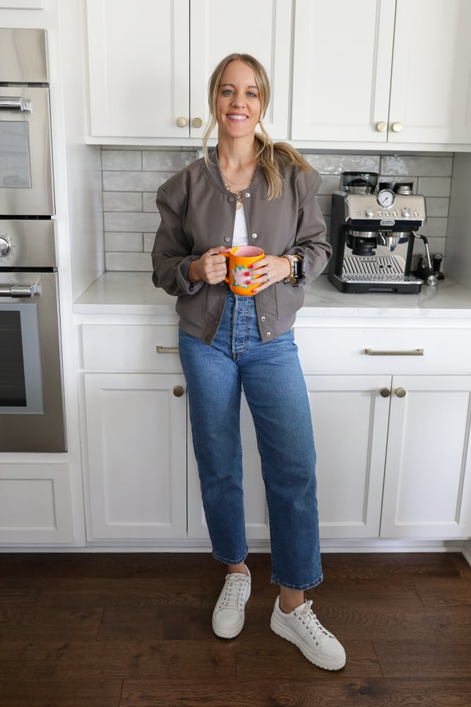 Woman in jeans, a white tank and bomber jacket.