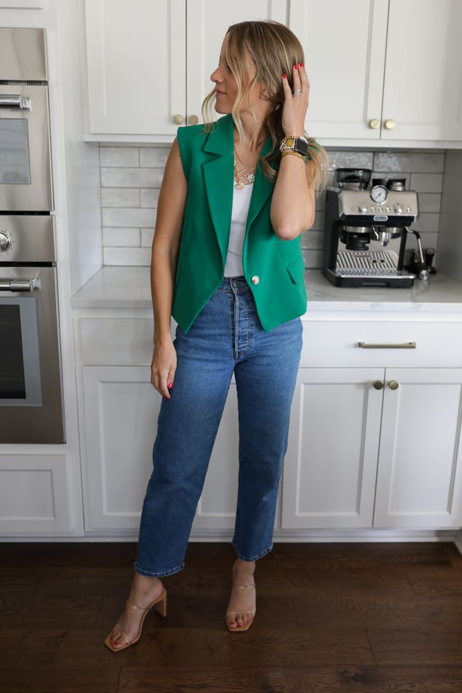 Woman in jeans, a white tank and sleeveless suit vest.