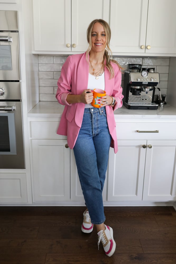 Woman in jeans, a white tank and pink blazer.