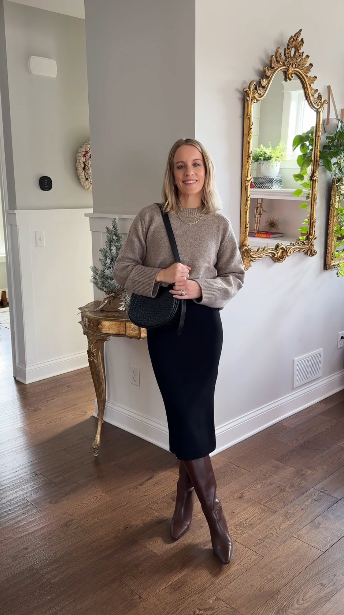 woman wearing neutral crew sweater, black midi dress, black purse, and leather boots