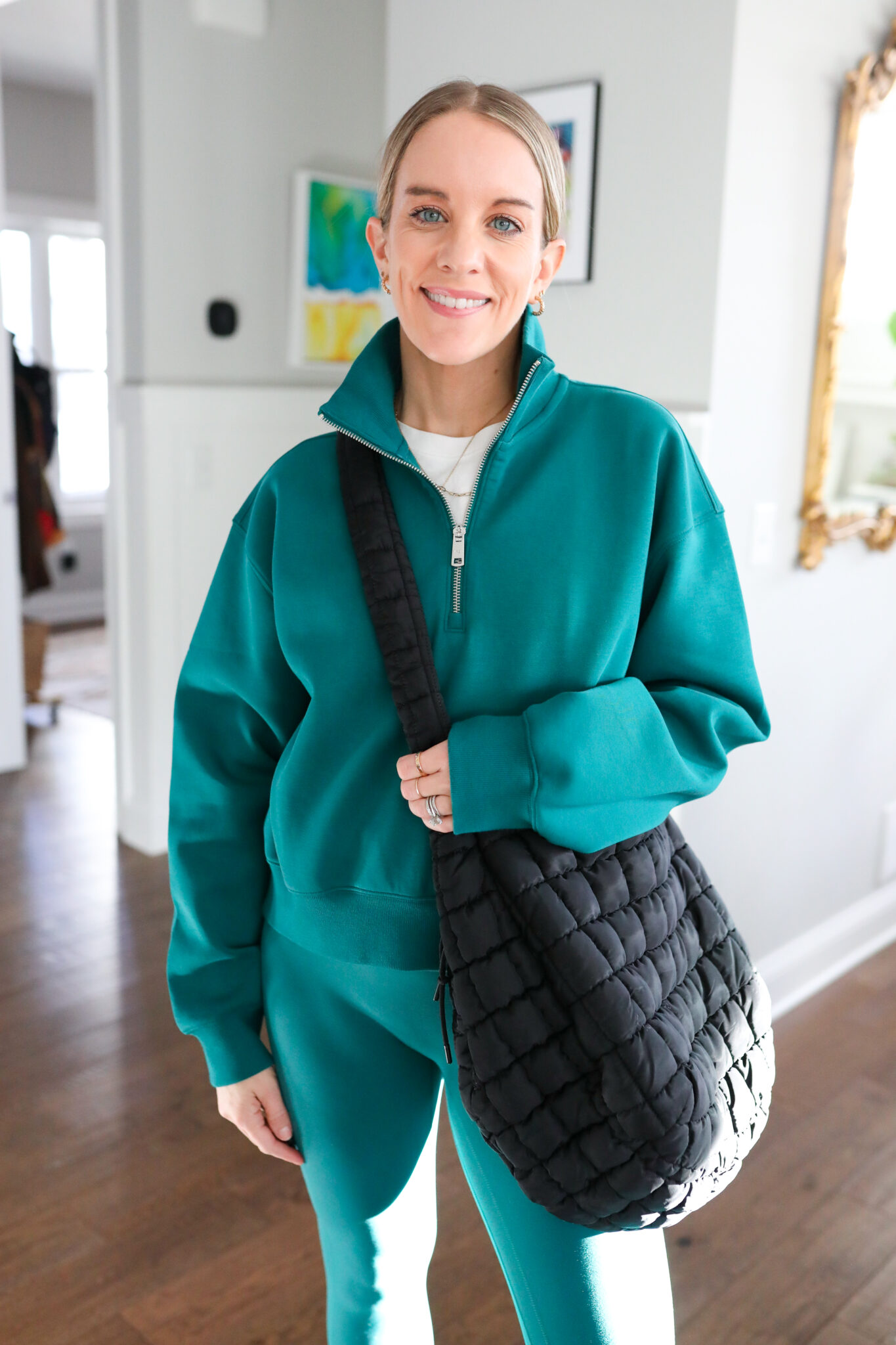 woman wearing green half zip pullover, green leggings, and puffer tote bag.