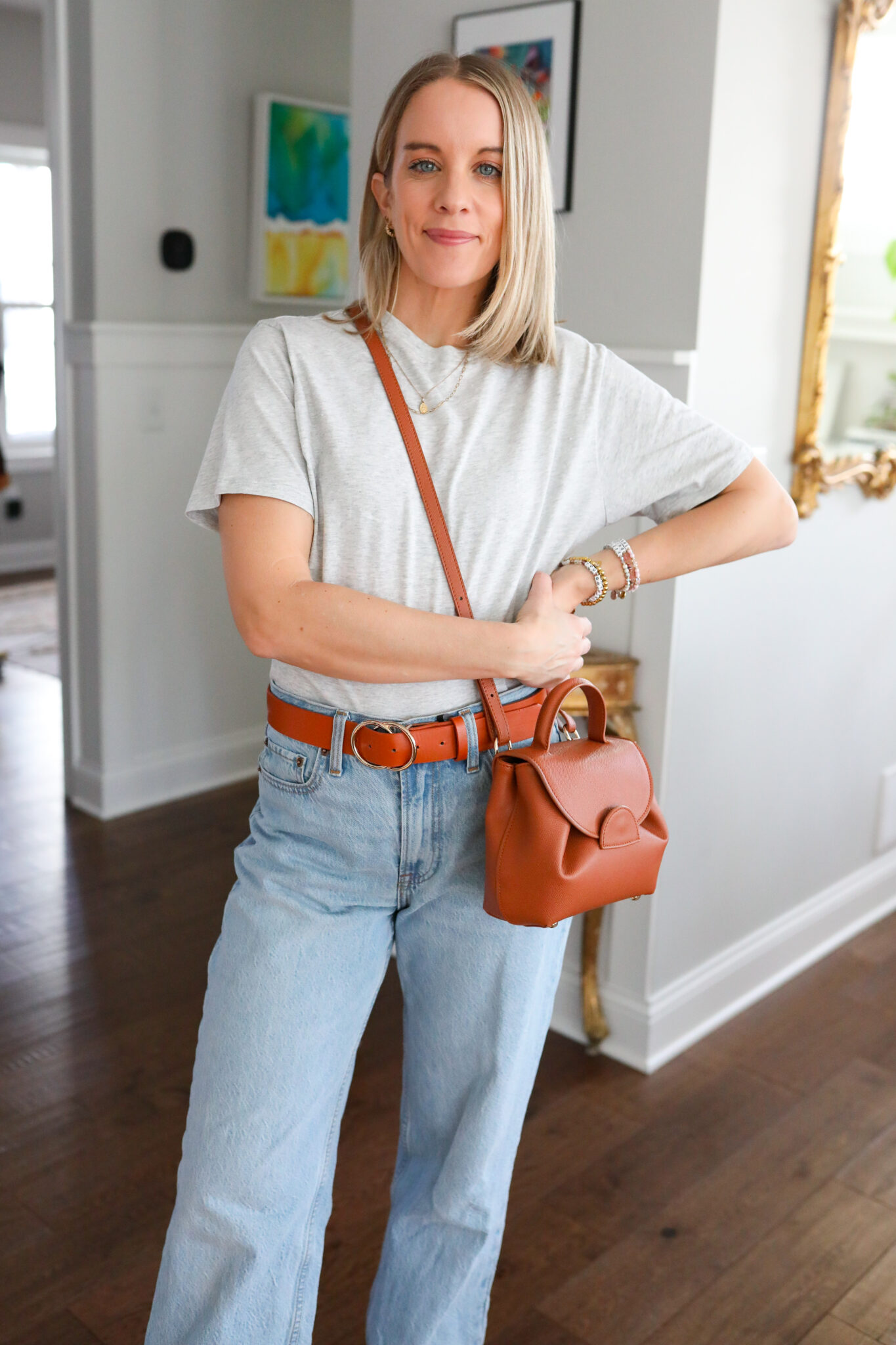 woman wearing Abercrombie gray tee, wide leg jeans, brown belt, and brown cross body bag.