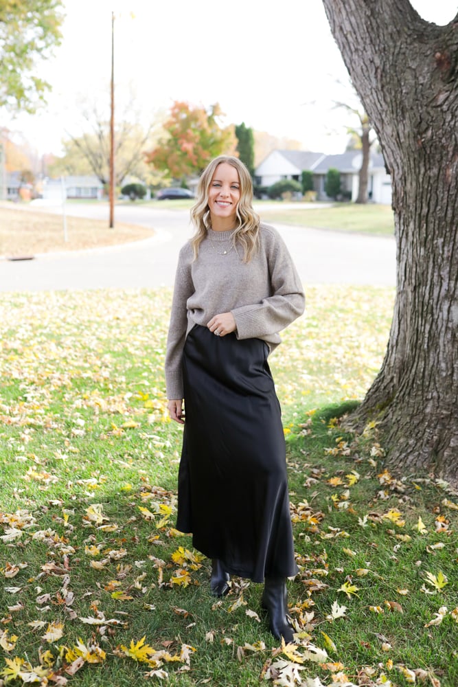 woman wearing a crew neck sweater, satin midi skirt, black boots