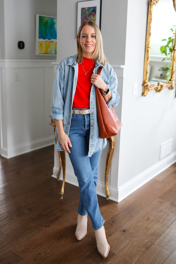 woman wearing denim button down, red tee,straight leg jeans, booties, and a tote bag.
