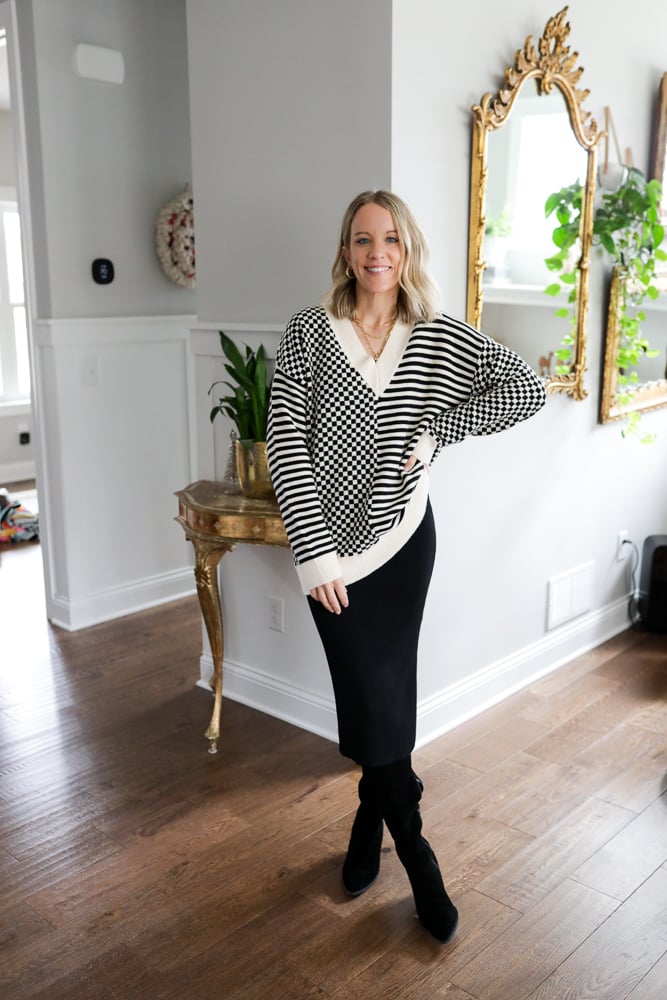 woman wearing a patterned black and white sweater, black midi dress, and boots