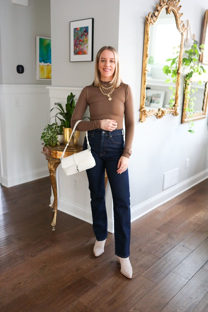 woman wearing brown long sleeve, denim jeans, white purse, gold jewelry, and booties