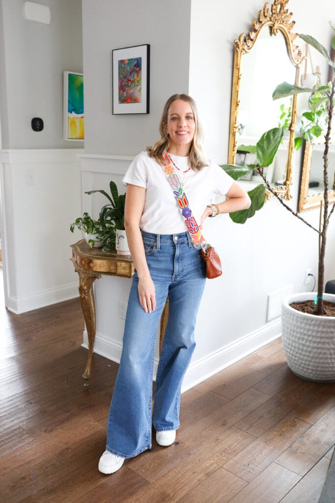 Woman wearing bell bottoms with white top and colorful purse.