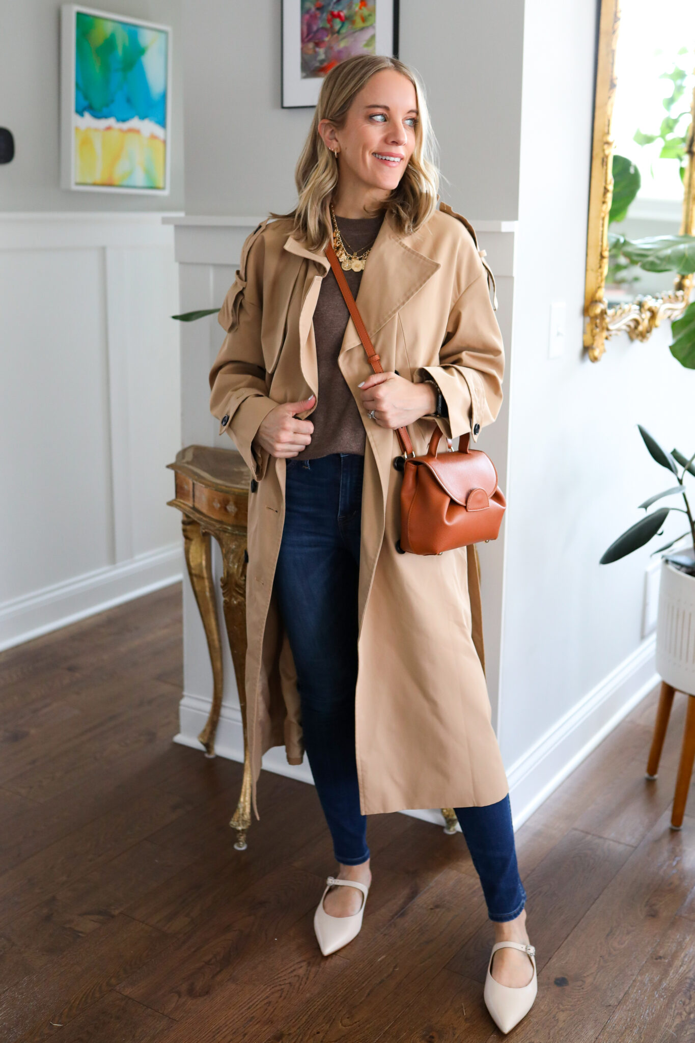 Woman wearing a trench coat over a brown top and jeans paired with neutral pointed toe flats 
