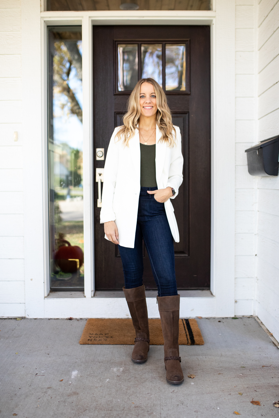 Woman wearing a white blazer over green tank with jeans and brown boots