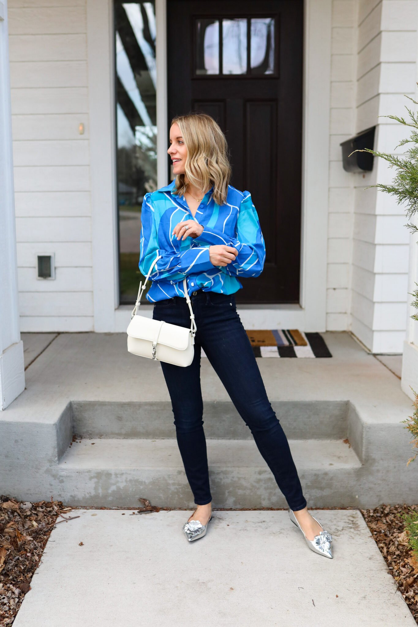 Woman wearing blouse tucked into jeans, paired with a cream bag and silver shoes