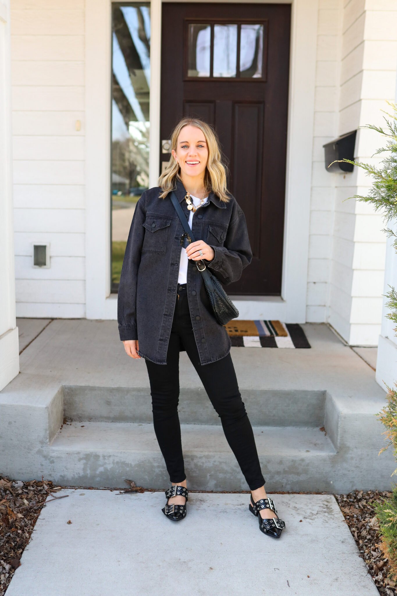 Woman wearing a denim like jacket over a white tee, paired with skinny black jeans and black sandals 
