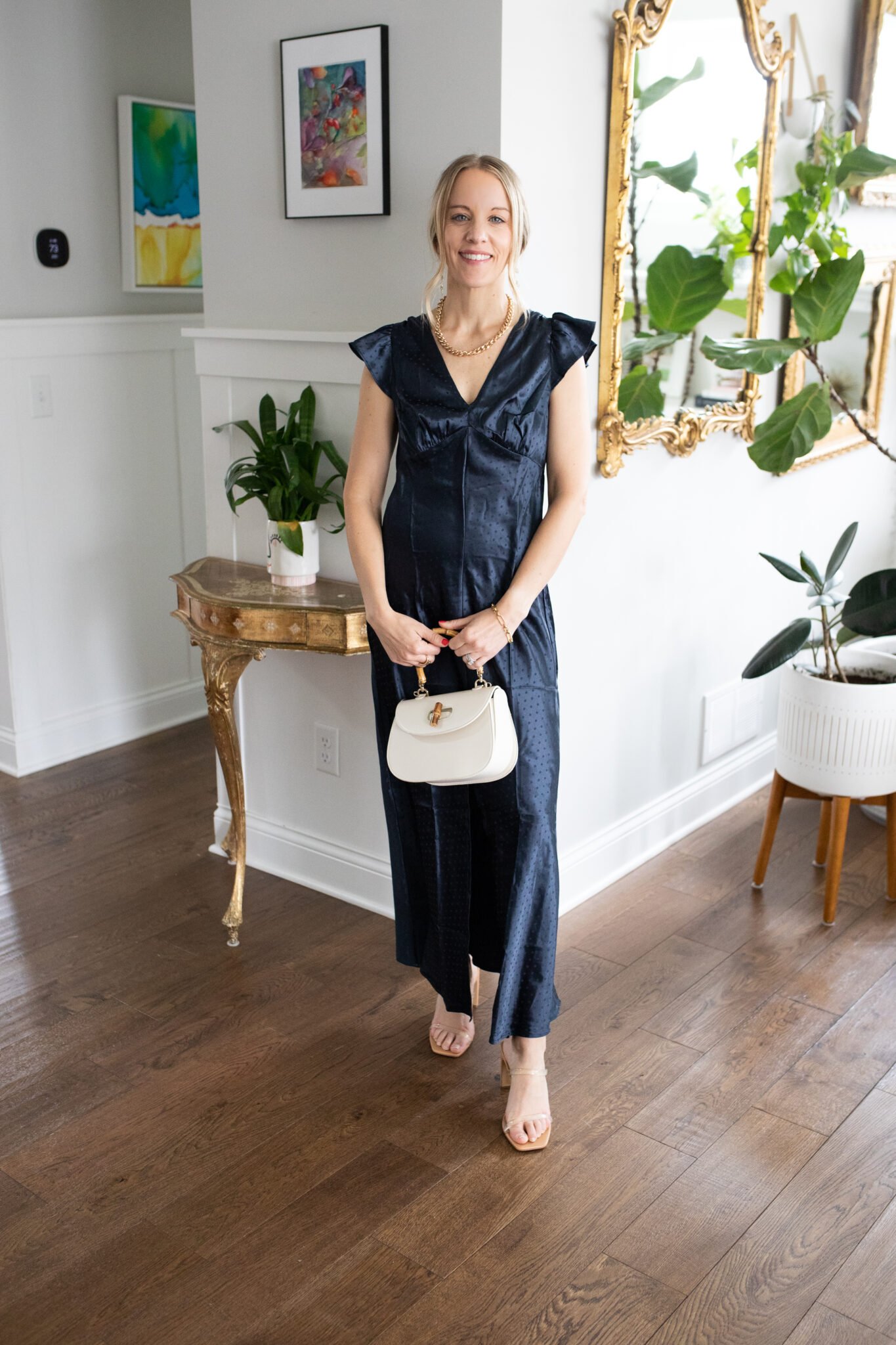Satin flutter-sleeve maxi dress with a deep V-neck and tonal dots, paired with a chic handbag and clear heels