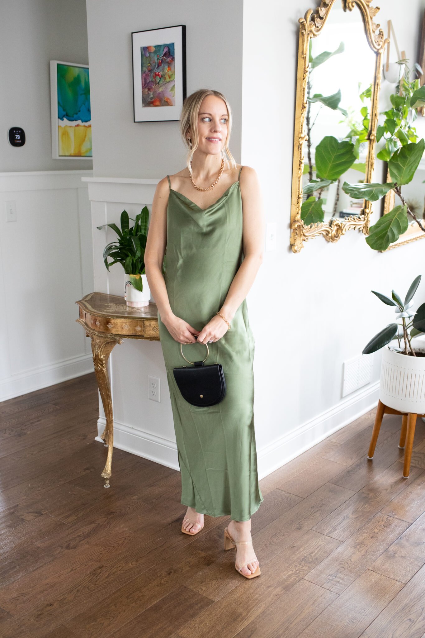 Green satin cowl-neck maxi dress with adjustable tie back, paired with clear heels and a chic handbag.
