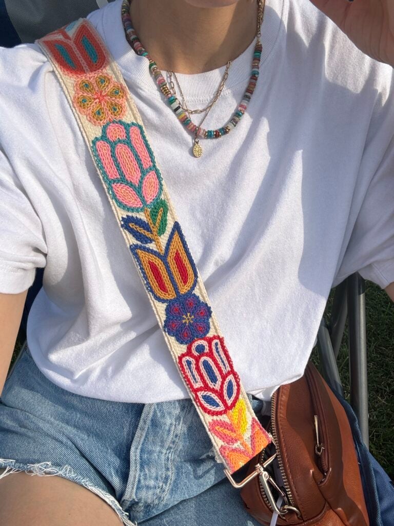 Woman in white t-shirt and cut off shorts with colorful bag strap and necklace stacks